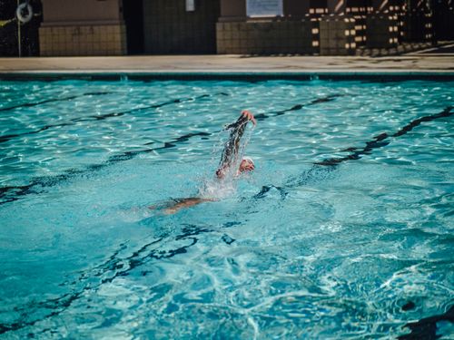 Free Adult man practicing freestyle swimming in a refreshing outdoor pool setting. Stock Photo