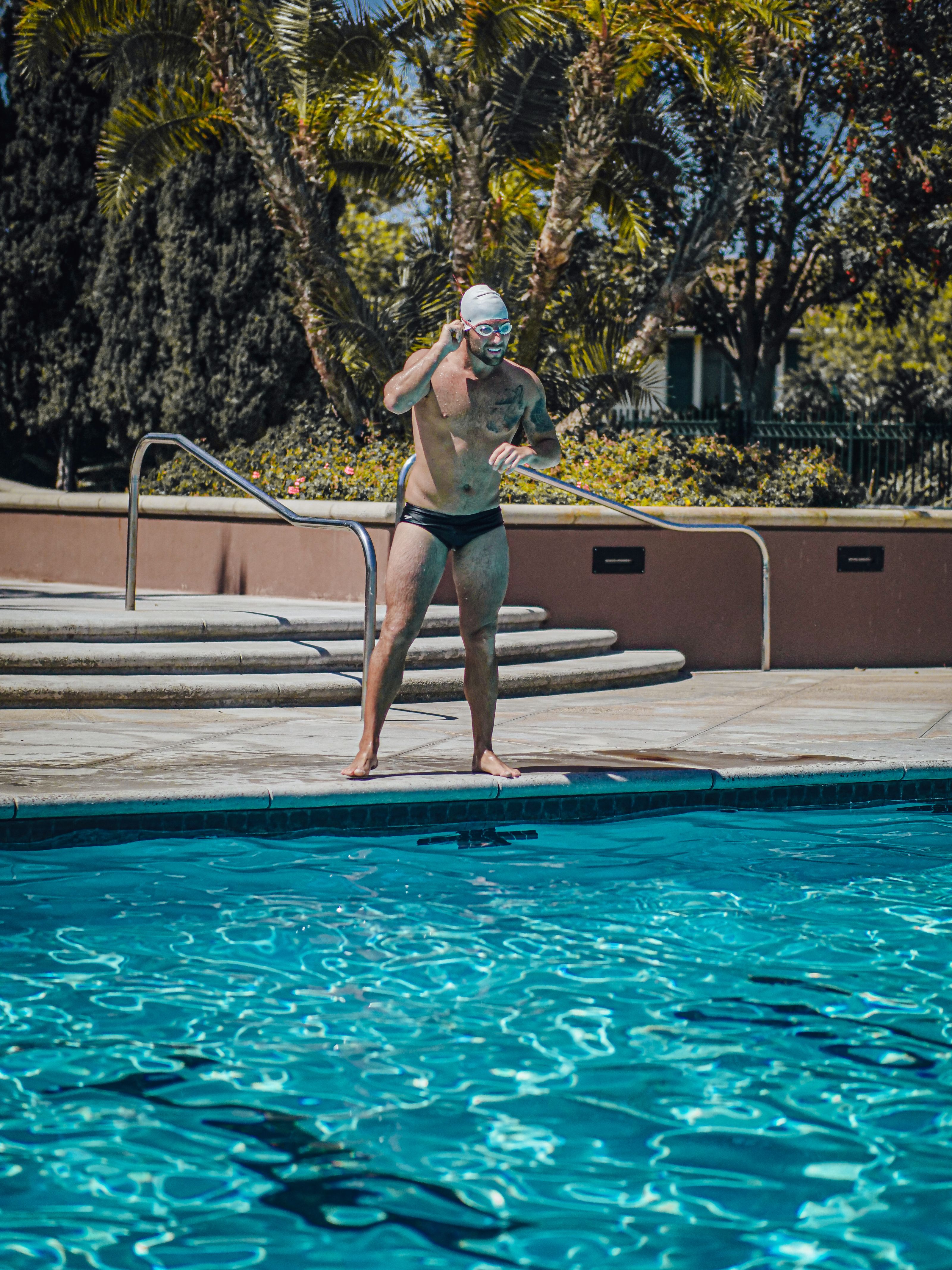 Nadador adulto usando óculos e touca pronto para mergulhar na piscina externa.