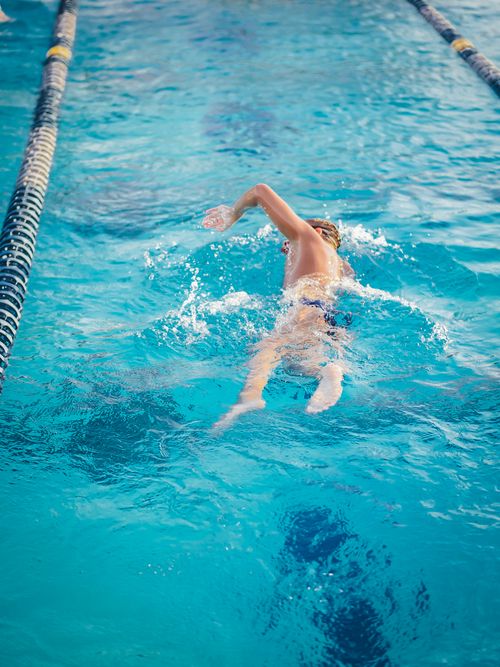 Free Young male swimmer in action, performing a freestyle stroke in a clear blue pool, representing fitness and athleticism. Stock Photo