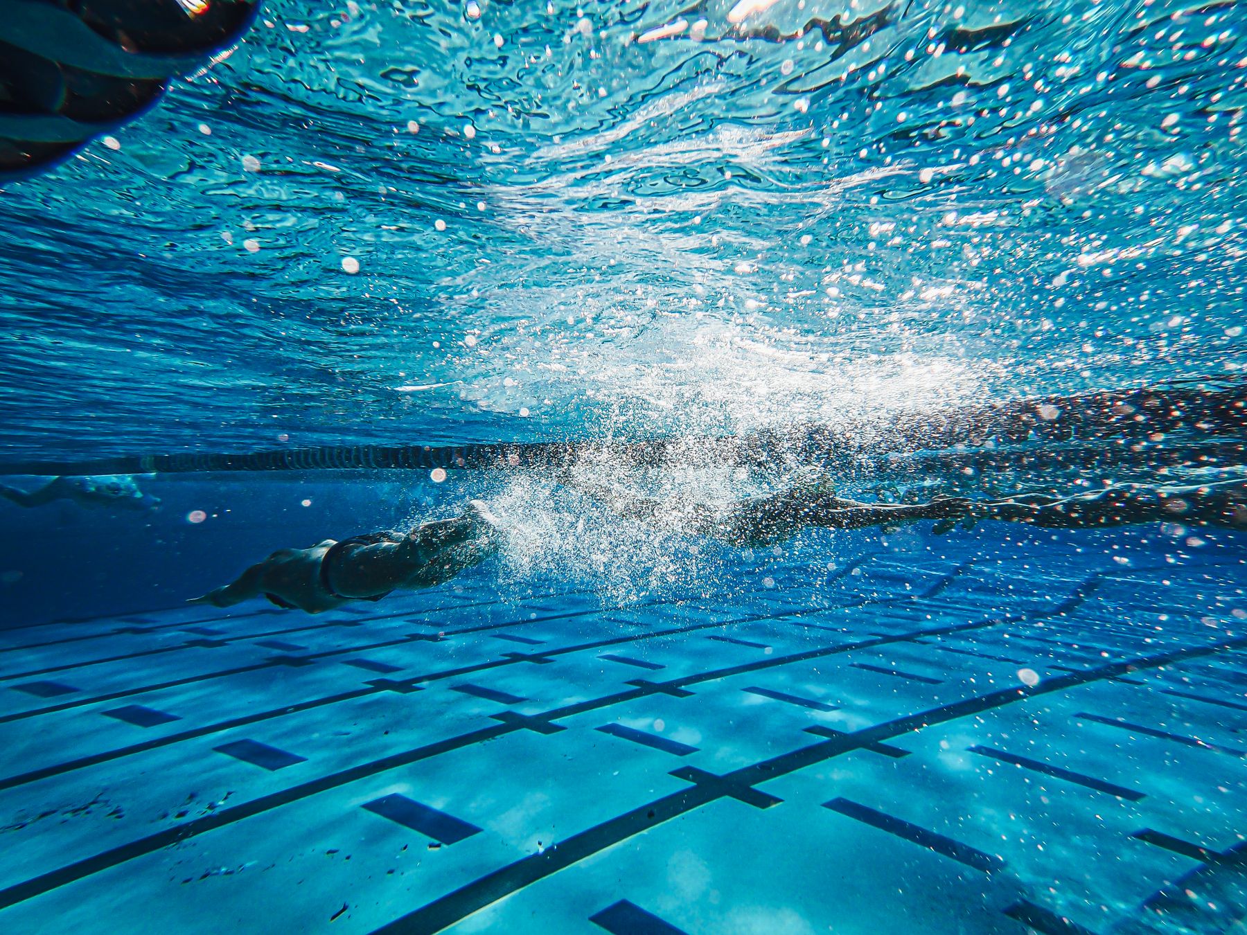 Swimmer photographed underwater mid-freestyle stroke, trailing bubbles in a blue pool