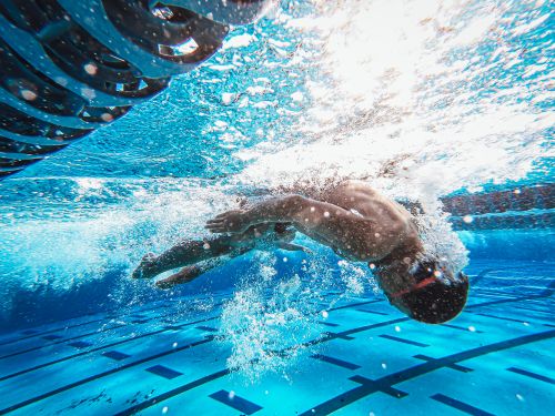 Free Dynamic underwater view of a man swimming freestyle in a clear blue pool. Stock Photo
