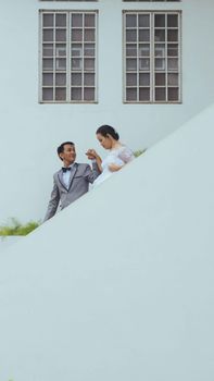 An Asian couple in wedding attire gracefully descends stairs, symbolizing love and unity.