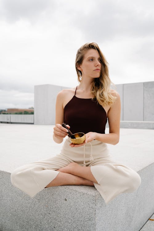 Free A Woman in Yoga Position Holding a Singing Bowl while Looking Afar Stock Photo