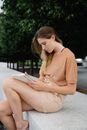 Woman in Brown Long Sleeve Shirt Sitting on Gray Concrete Bench Reading Book