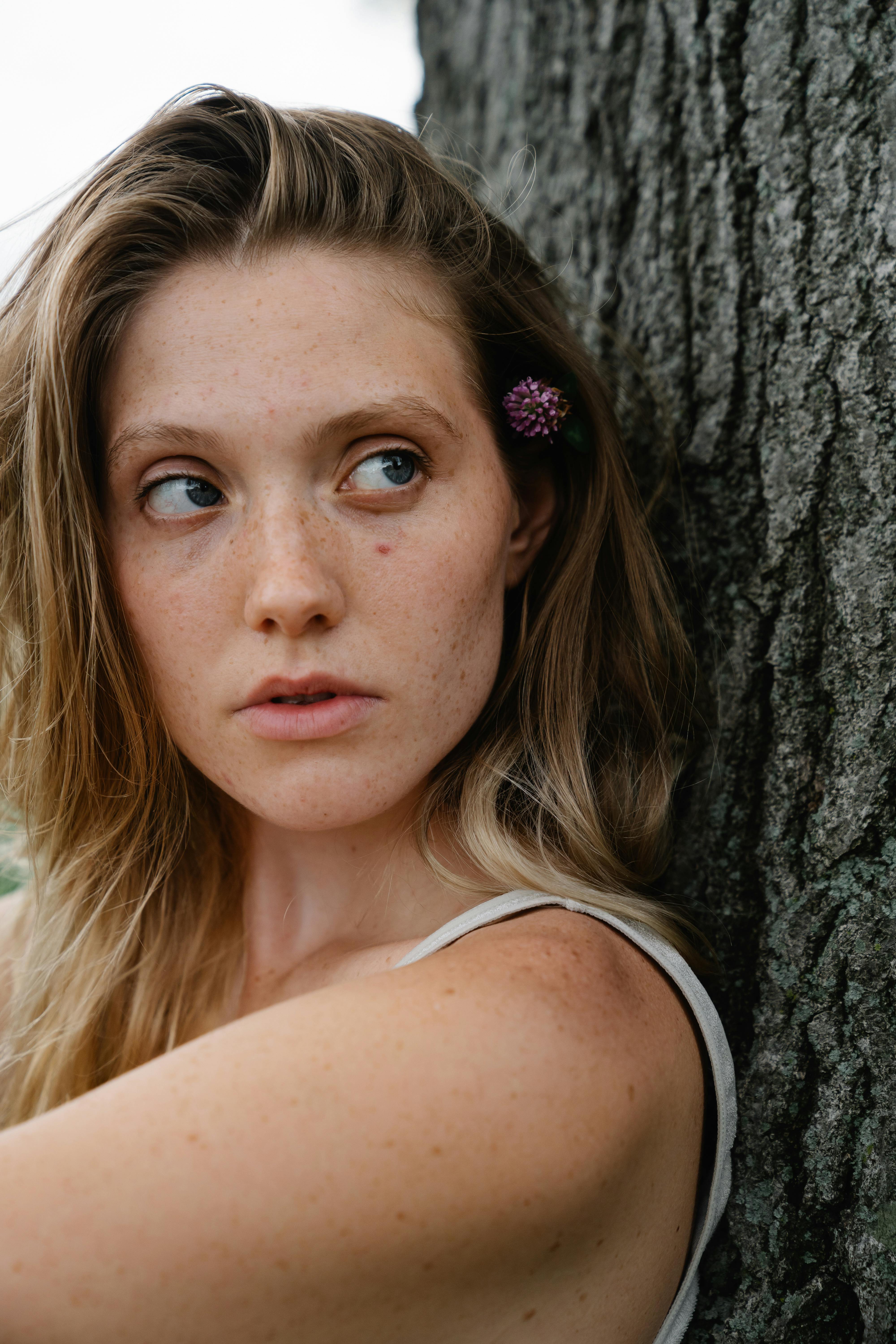 a beautiful woman with flower on her ear leaning on a tree trunk while looking afar