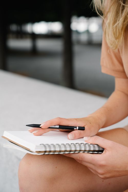 Free Close-up of a woman writing in a spiral notebook outdoors with a pen. Stock Photo