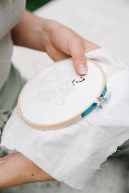 Close-up of hands working on punch needle embroidery with a wooden hoop