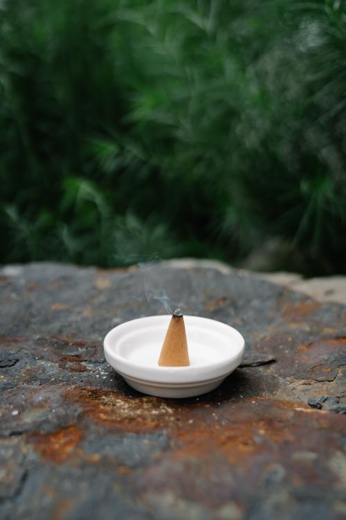 Free A calming scene featuring a cone incense burning in a ceramic bowl, set on a stone surface outdoors. Stock Photo
