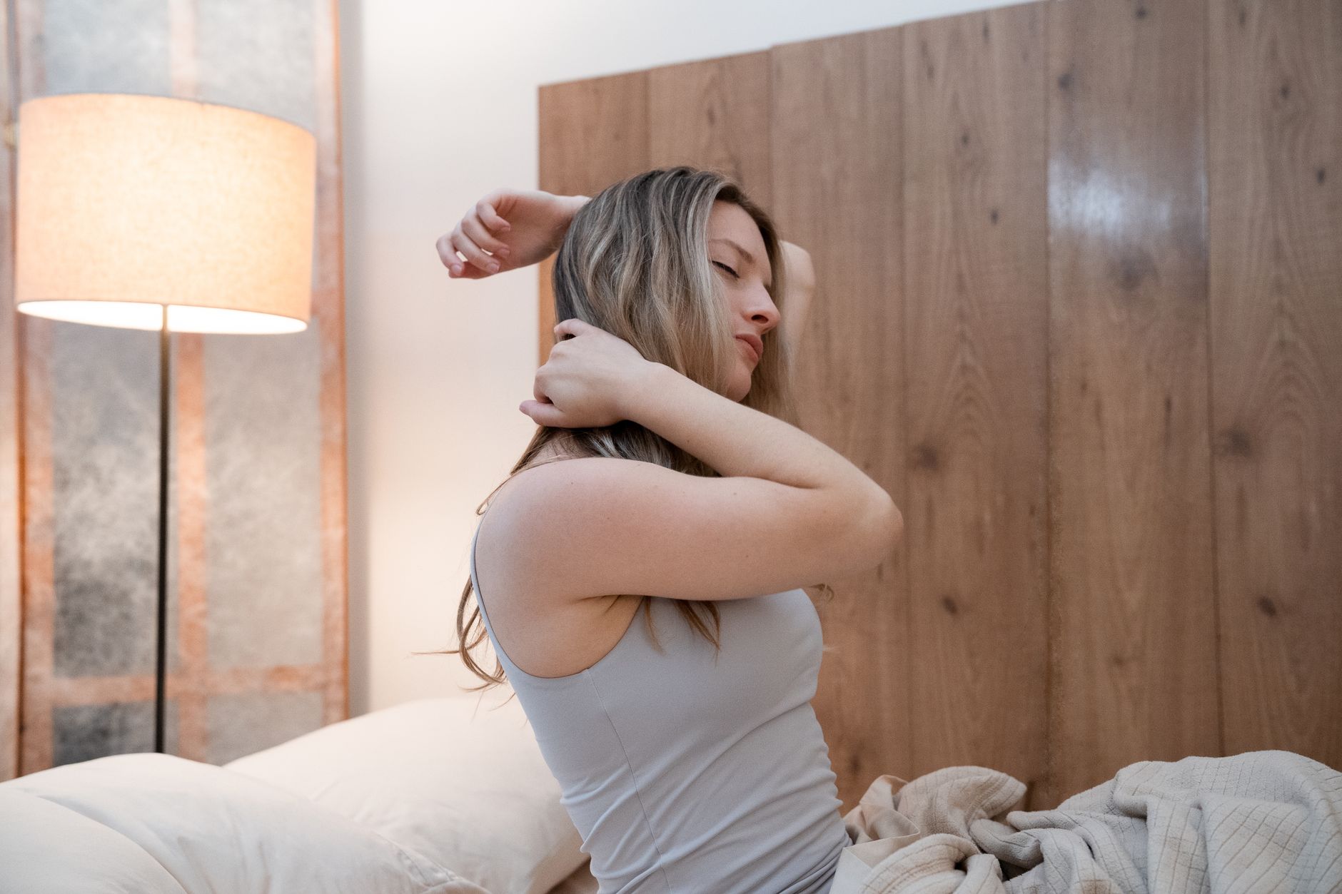 woman waking up refreshed and stretching peacefully in soft morning light with white bedding and a calm, minimal bedroom background