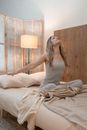 Woman in White Tank Top and White Pants Sitting on Bed