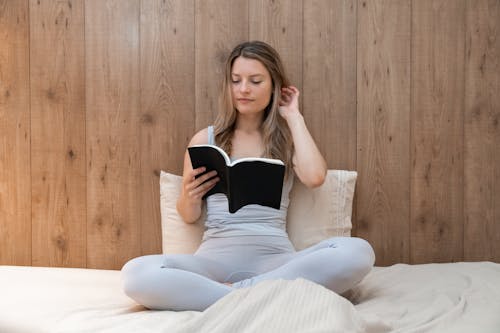 Free A Woman Reading a Book while Sitting on the Bed Stock Photo