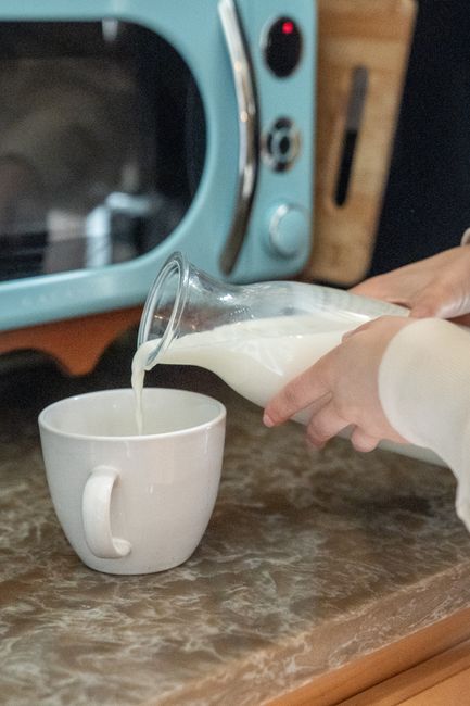 A glass pitcher pouring thick white sweet cream into a bowl, with visible richness and a faint sheen on the surface