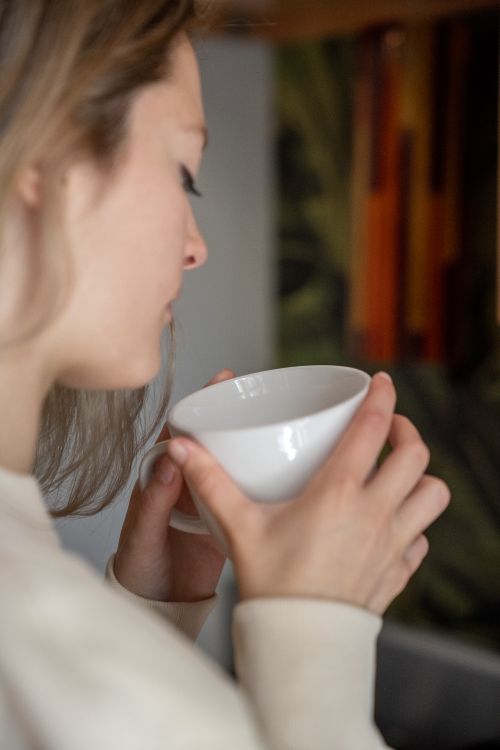 Free Side profile of a woman holding a white mug, enjoying a hot drink indoors. Warm and cozy atmosphere. Stock Photo