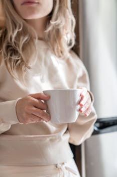 A woman in casual attire holding a white mug indoors, adding warmth and comfort to the scene.