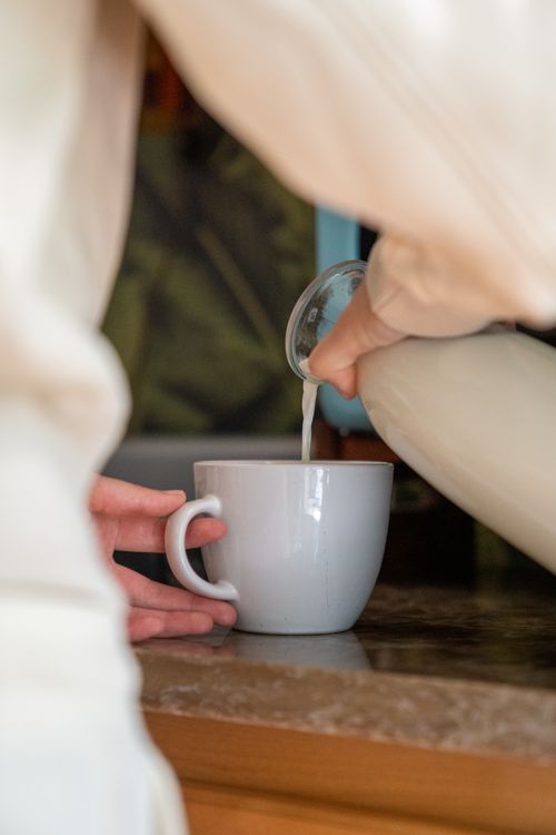 Free Close-up of milk being poured into a white cup on a kitchen counter with hands involved. Stock Photo