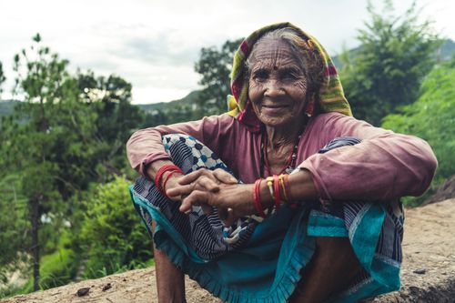 Free Smiling elderly Indian woman in traditional attire sitting outdoors in nature. Stock Photo