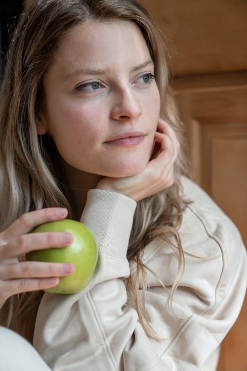 A Woman with Her Hand on Her Chin Holding a Green Apple