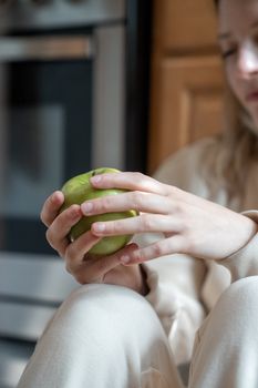 Woman's hands gently holding a green apple indoors with a soft background focus.