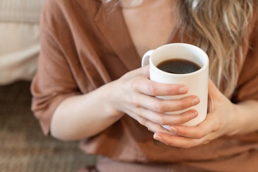 Close-up of a person holding a white mug filled with black coffee, showcasing a cozy and relaxed atmosphere.