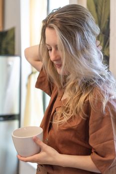 Woman with blonde hair holding a ceramic cup, relaxing at home.