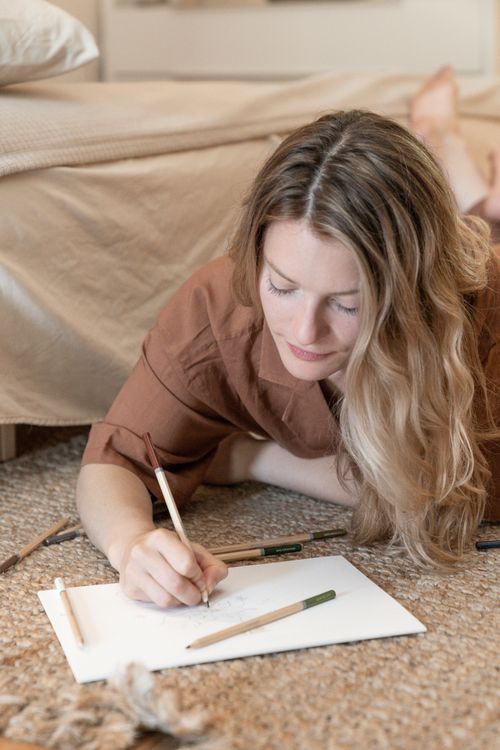 Free Caucasian woman drawing with colored pencils on paper indoors. Bright and relaxed setting. Stock Photo