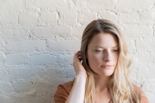 Woman in Brown Shirt Touching Her Hair