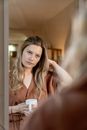 Woman in Brown Shirt Looking in the Mirror Holding a White Ceramic Mug