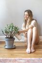 Woman Sitting on Floor Watering Plant