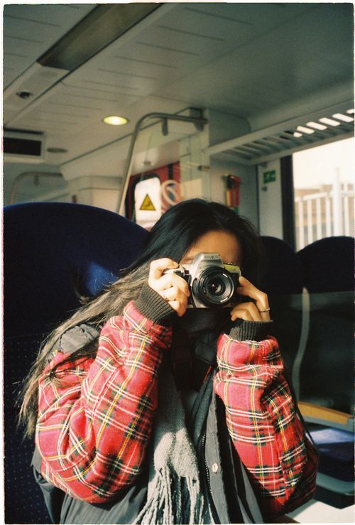 Free A woman in a plaid jacket takes photos inside an Amsterdam train, capturing candid moments. Stock Photo