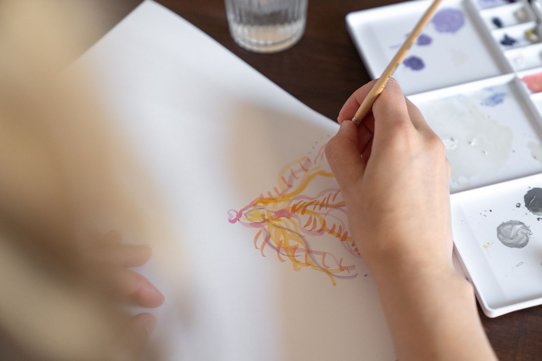 Close-up of a hand painting with watercolors, creating intricate designs on paper.