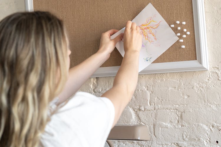 Woman Pinning Drawing On Pin Board