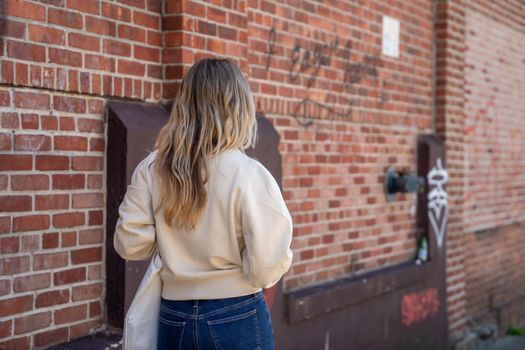 Woman in Beige Long Sleeve Shirt and Blue Denim Jeans Standing Near Brown Brick Wall during