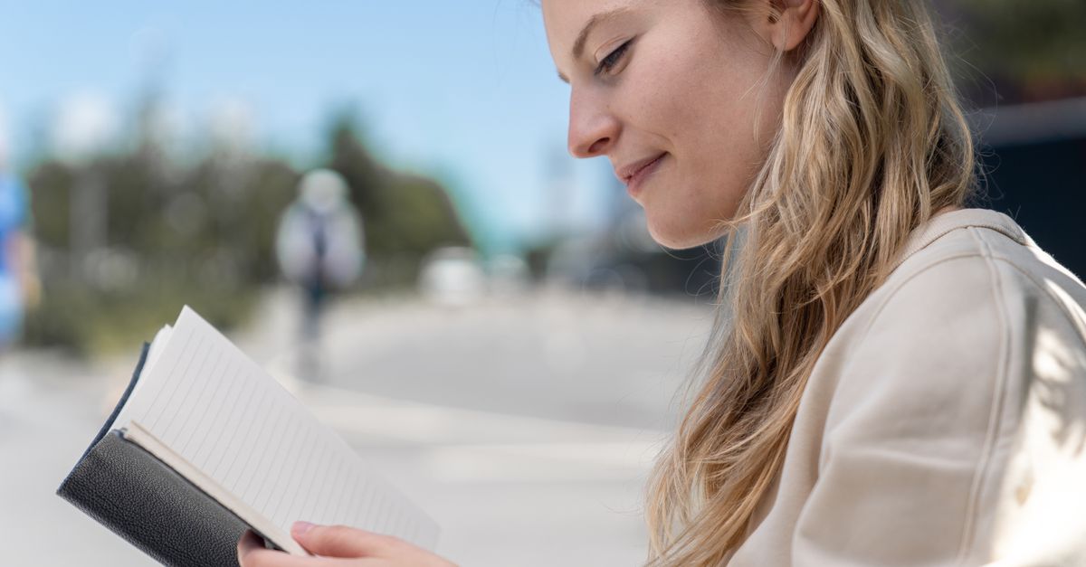 person ignoring phone notifications while reading a physical book in a sunny park
