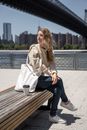 Woman Sitting on Wooden Bench with Her White Shoulder Bag and Coffee Drink