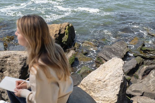 Woman Sitting on Rock Near Body of Water 