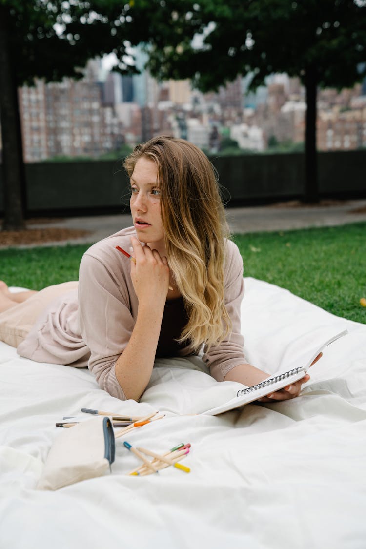 Woman Lying In Park Writing In Notebook