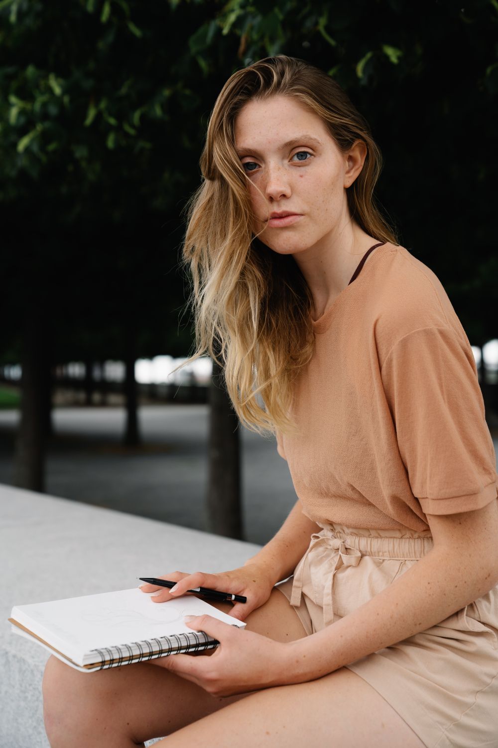Woman sitting outside with a notebook and pen, writing amid greenery