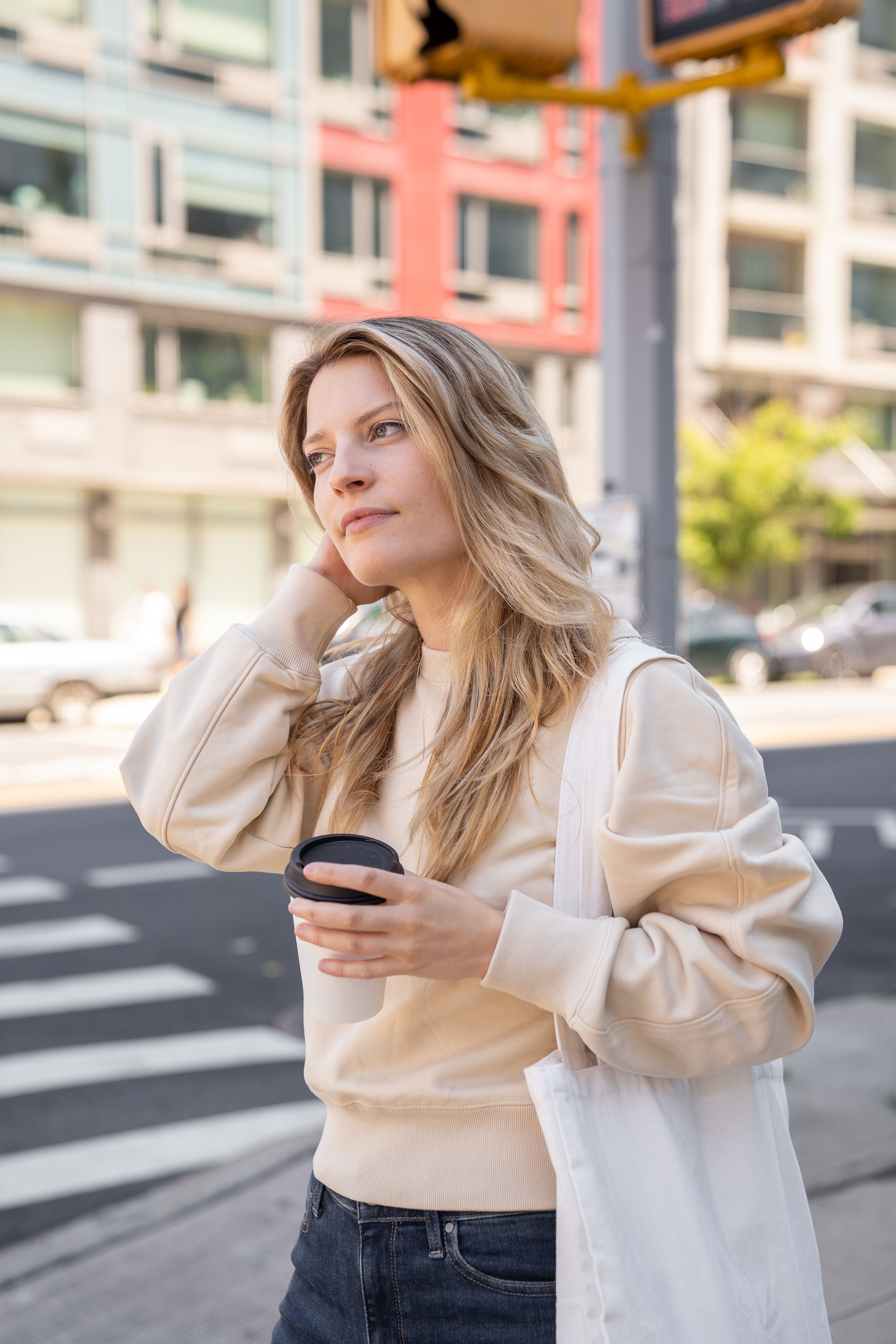 A woman with blonde hair holds a coffee cup while walking in an urban setting.