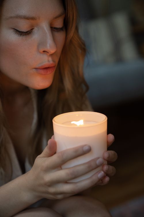 Free Young woman gently blowing a candle flame indoors, creating a serene ambiance. Stock Photo