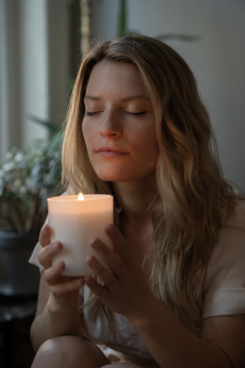 Free A serene woman with closed eyes savoring a lit candle's scent indoors. Stock Photo