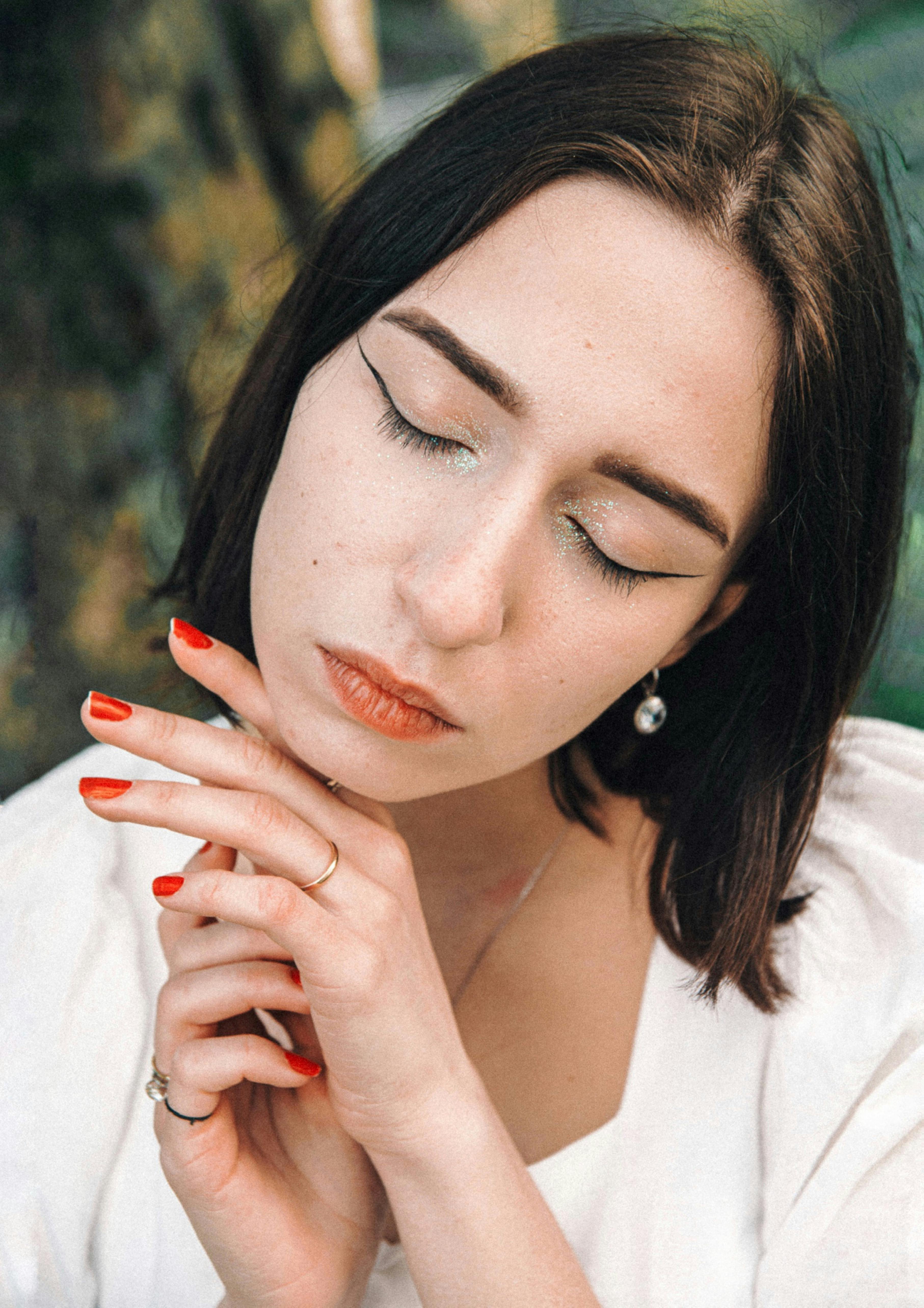 Close-up portrait of a woman with elegant makeup, eyes closed, and serene expression against a natural background.