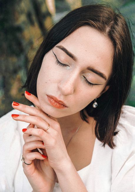 Close-up portrait of a woman with elegant makeup, eyes closed, and serene expression against a natural background.