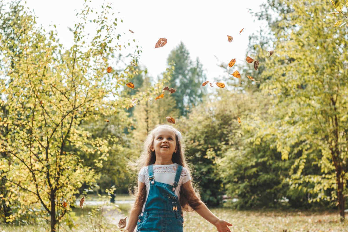 A happy child playing in falling autumn leaves in a sunny park