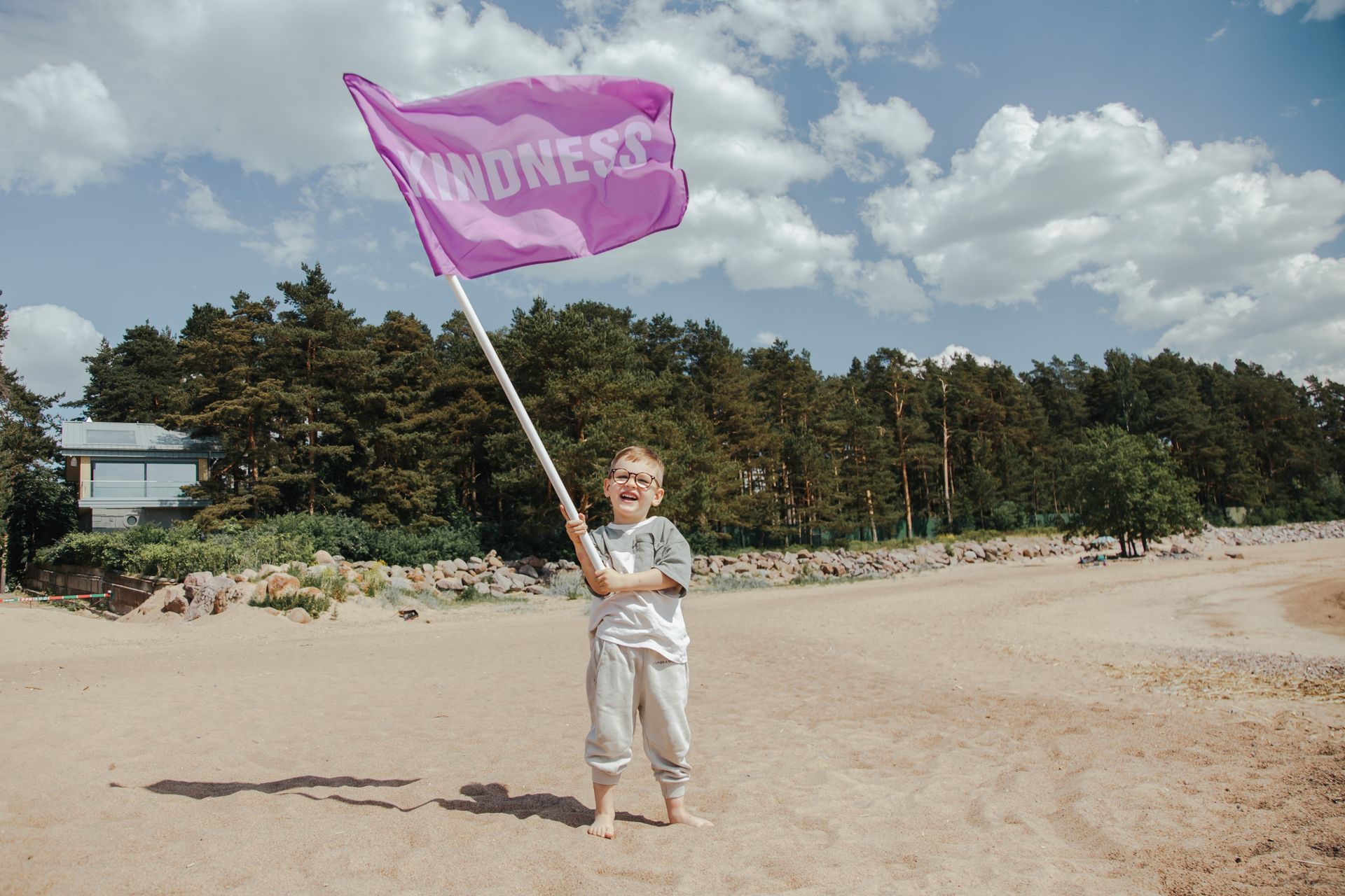 A joyful child waving a 'Kindness' flag on a sunny beach, embracing positivity and fun.