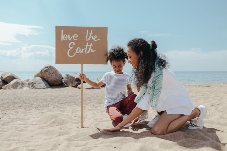 A Woman And A Child Holding A Poster On The Beach