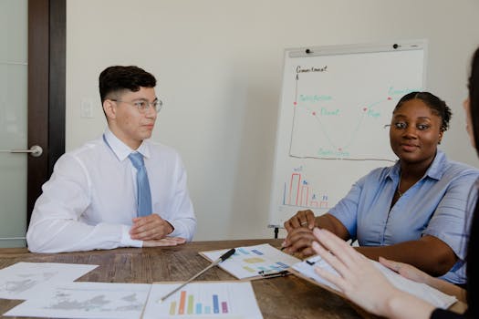Asian man and black woman engaged in a strategic office meeting, discussing charts and data.