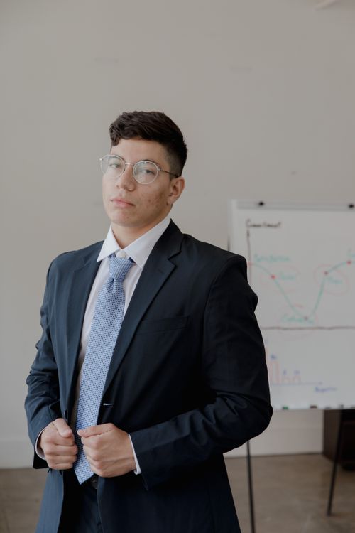 Free Confident young adult in black suit indoors near flip chart. Stock Photo