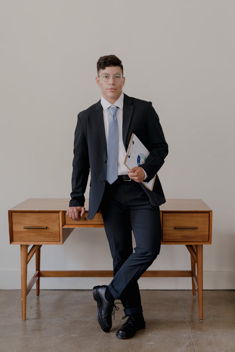 A Well Dressed Man Leaning On A Wooden Desk