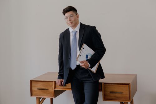 Free Professional man in a suit with a clipboard smiling confidently indoors. Stock Photo