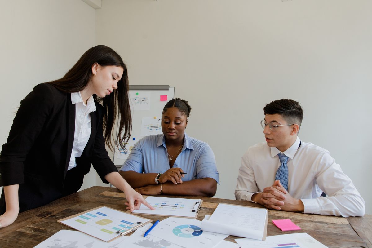 A woman pointing at charts on a table while two colleagues look on